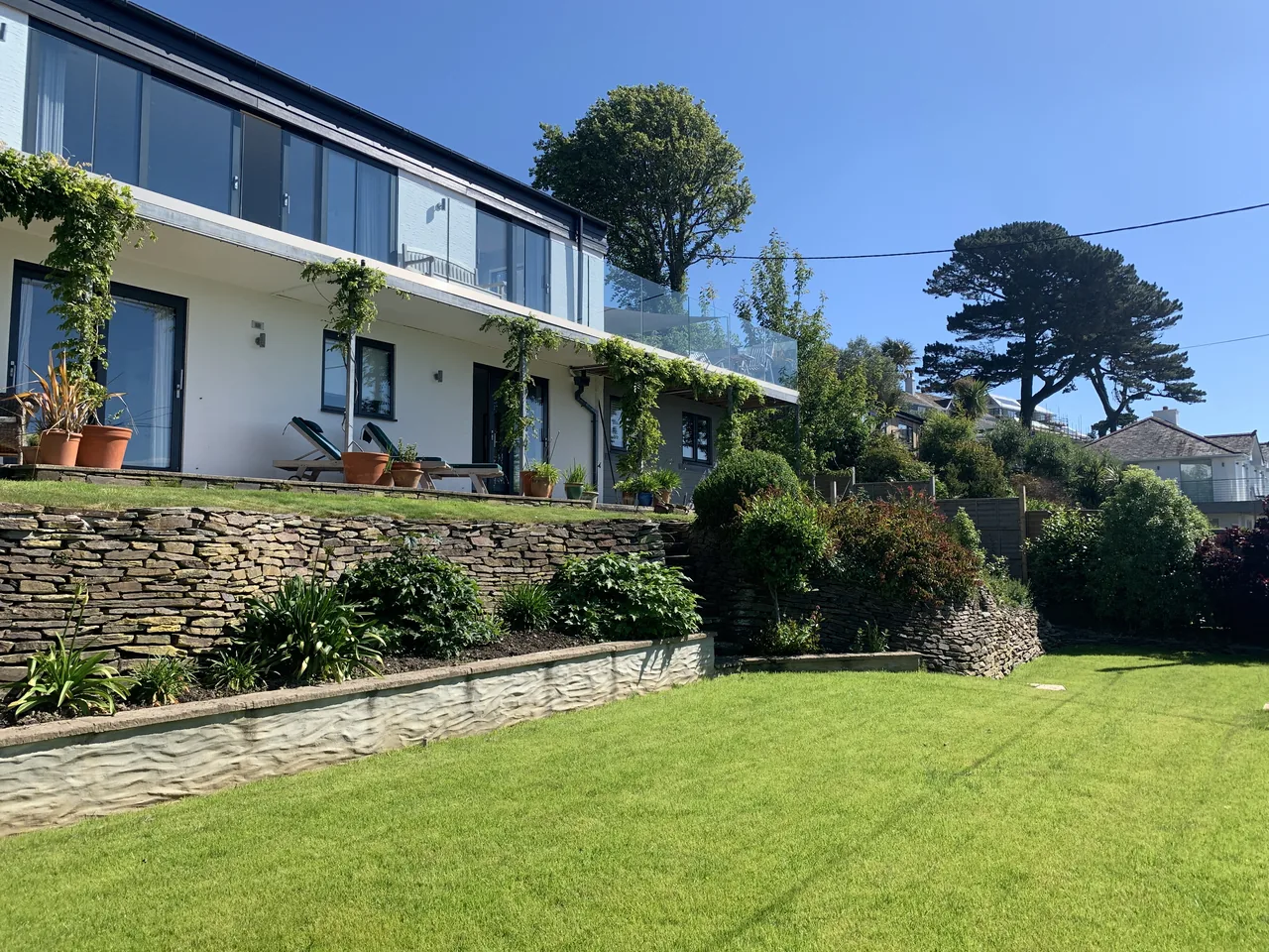 The white house above a lawn, planted terraces and stone retaining walls.
