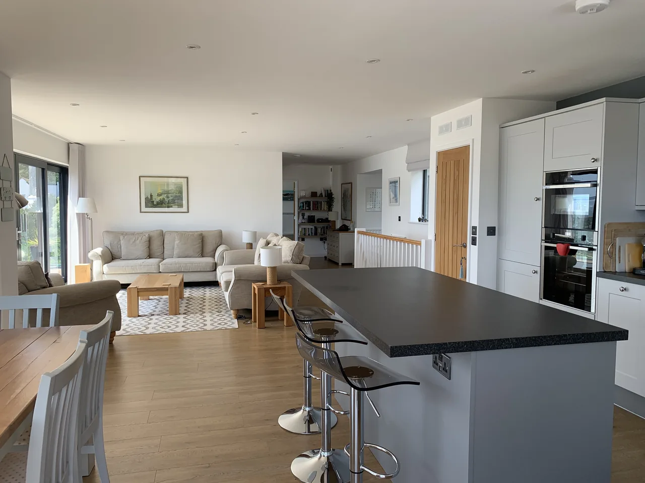 A kitchen island and dining table with sofas beyond, in a room with wooden flooring.