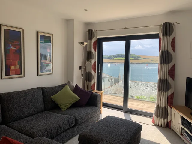 A dark sofa beside a glass door looking towards the water, with framed pictures on the wall.
